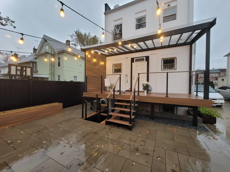 A raised deck, cable railings, a privacy screen and warm lighting.