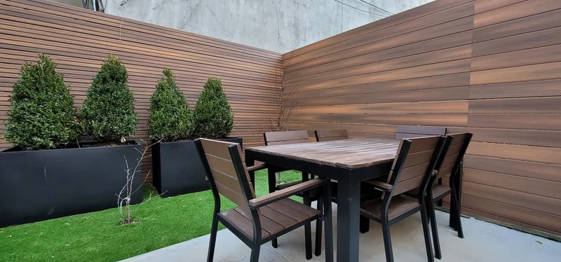 Horizontal screening and planted borders frame a garden dining area.